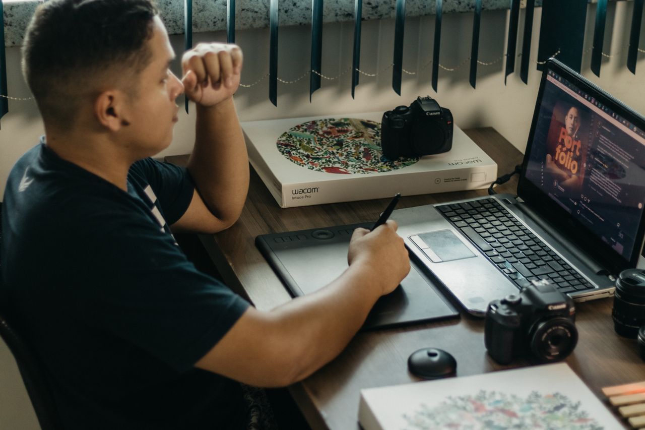Un photographe qui travaille dans un espace créatif avec un ordinateur portable et une tablette Wacom, concentré sur la retouche photo en intérieur.